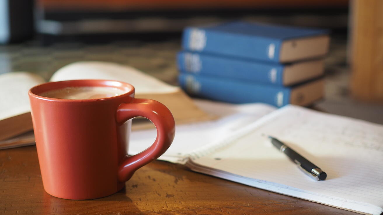 Skrivebok, kaffikopp og bøker.
