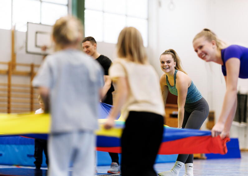 Lærerstudenter som har gymtime med unge elever på barneskolen inne i en gymsal